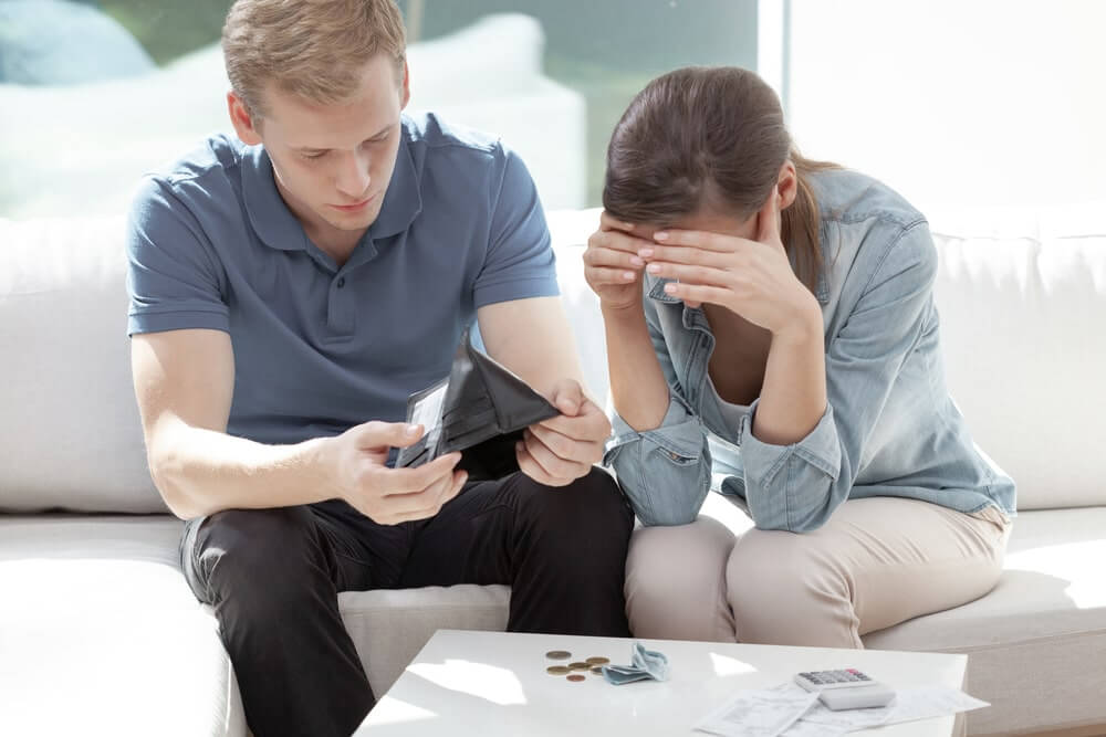 poor couple sitting on the couch with open wallet